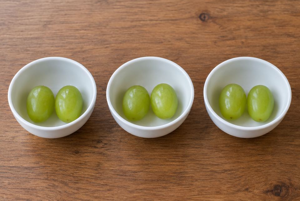 Three small white bowls in a row, each with two green grapes.