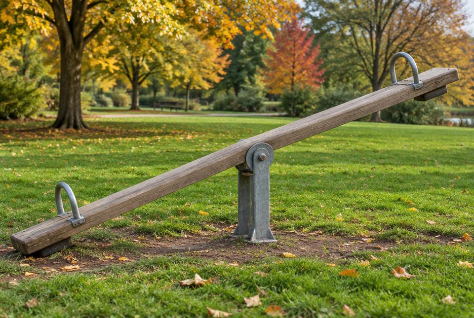 A wooden seesaw in a park in autumn, with one end down on the ground and the other end up in the air.