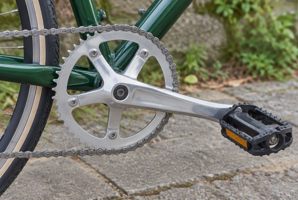 Close-up of a bicycle's pedal, crank arm, toothed front sprocket and chain.