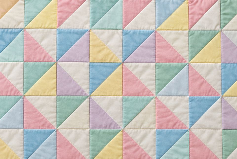 A pastel patchwork quilt made of many same-sized triangle pieces.