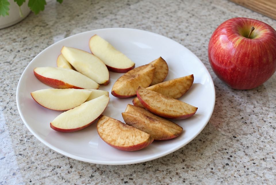A plate of apple slices: some are still pale on the cut side and others have turned brown, with a whole red apple beside the plate.