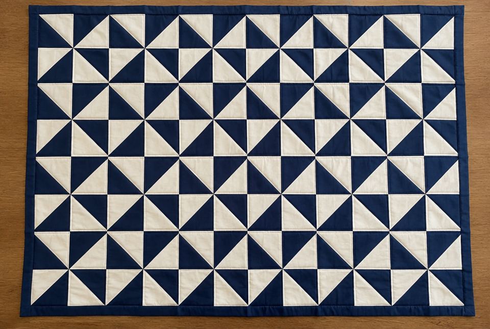 A navy and cream quilt covered in pinwheel blocks made from right triangles.