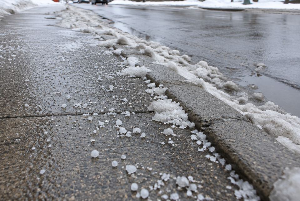 A wet sidewalk scattered with white road-salt crystals beside melting slush and a curb.