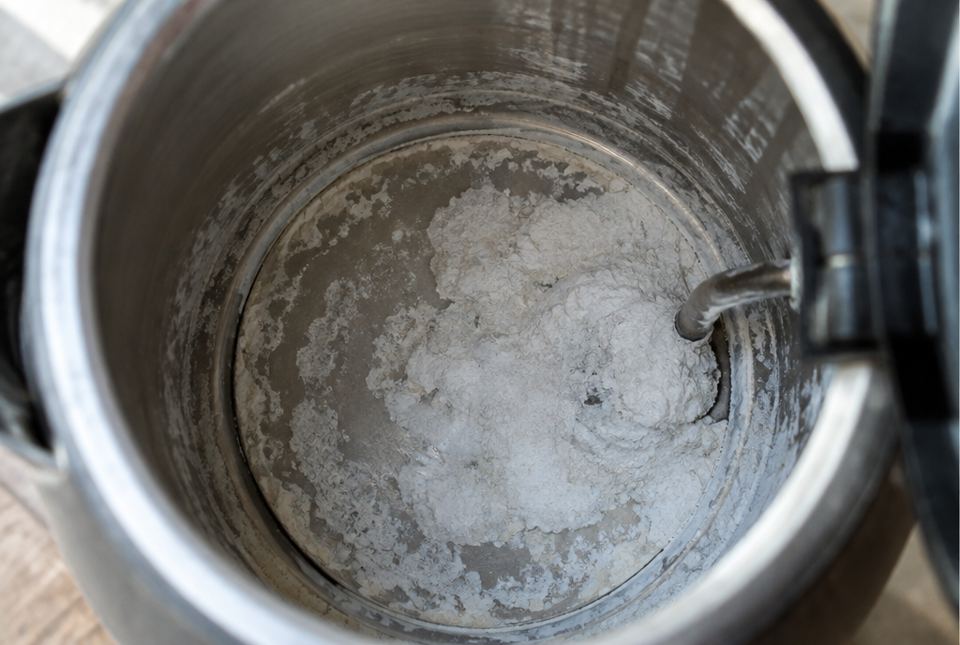 Looking down inside an old kettle with a white chalky crust on the bottom.