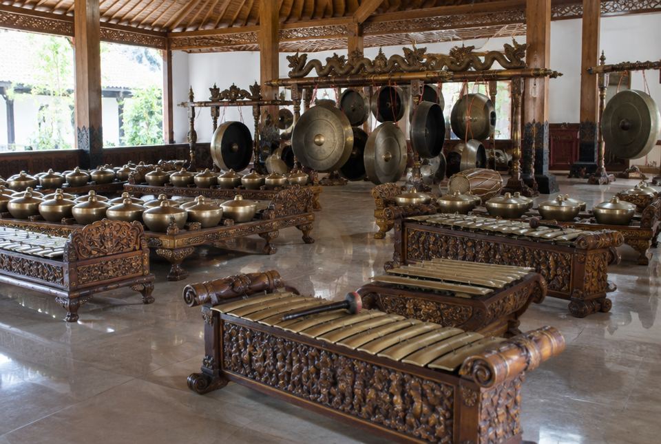 A full set of bronze gamelan instruments, with gong-chimes, metallophones and large hanging gongs, in carved wooden frames.